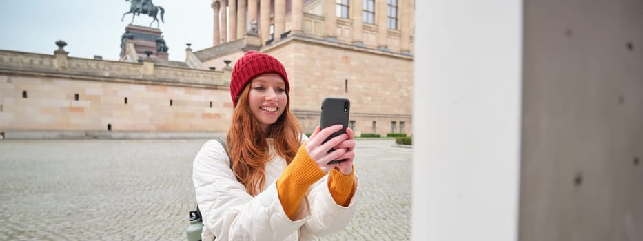 Smiling girl tourist takes photo of historical landmark, makes a photo on smartphone. Copy space