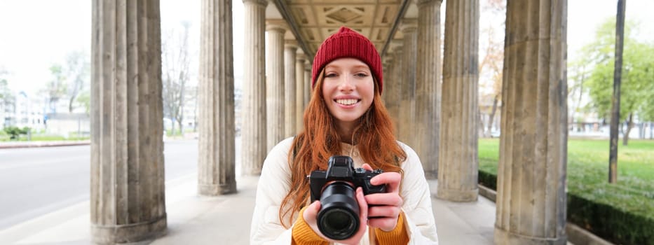 Smiling tourist photographer, takes picture during her trip, holds professional camera and makes photos. Copy space