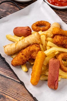 Snack plate with french fries, crispy chicken, cheese sticks, sausage and spring rolls on wooden table