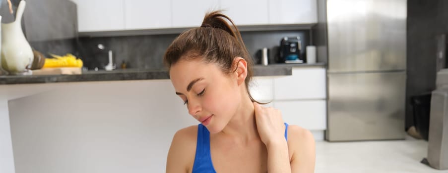 Image of woman workout at home, stretching her head and neck, does warm-up exercises before yoga, fitness training in living room.