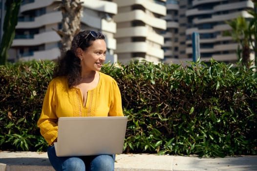 Portrait of a charming curly haired multi-ethnic young woman, entrepreneur, smiling looking aside, working remotely on new business project. People. Online business. Freelance job. Career. Success