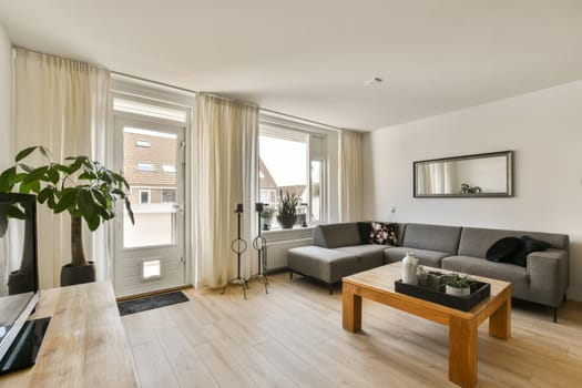 a living room with wood flooring and white walls, there is a grey couch in front of the window