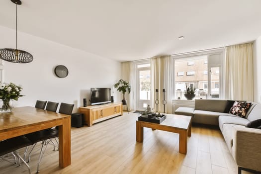 a living room with wood flooring and white walls, including a wooden dining table surrounded by black leather chairs