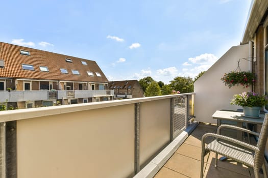 a balcony with chairs, tables and flowers on the railings in front of an apartment building under a blue sky filled with clouds