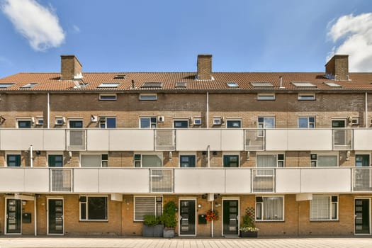 an apartment building with many windows and bales on the top floor, in front of it is a blue sky filled with white