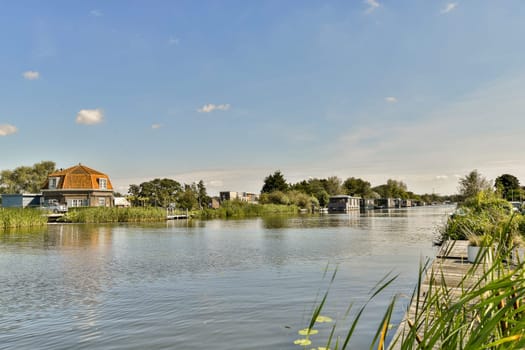 a body of water with houses in the background and green plants growing on both sides of the lake, surrounded by grass