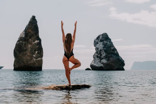 Woman meditating in yoga pose silhouette at the ocean, beach and rock mountains. Motivation and inspirational fit and exercising. Healthy lifestyle outdoors in nature, fitness concept.