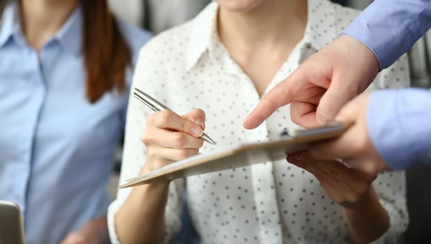 Close-up of smart people working in big modern office with smart manager. Trendy woman in classy blouse writing something in paper folder. Company meeting concept