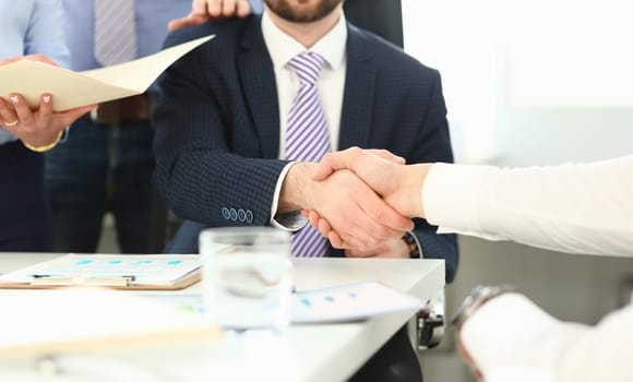 Focus on business male performing friendly gesture towards colleague. Smart man in classy suit shaking hands with young manager. Company meeting concept. Blurred background
