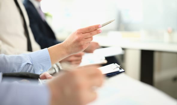 Focus on friendly colleagues discussing new business project. Gorgeous woman with pen pointing with writing utensil in big modern office building. Company meeting concept. Blurred background