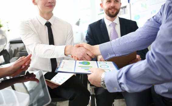 Close-up of smart colleagues smiling and shaking hand with prudent boss. Young manager giving important business project that determine future of corporation. Company meeting concept