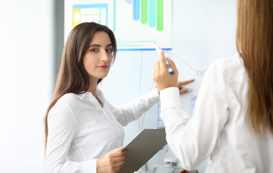 Portrait of smart businesswoman sitting in modern workplace and pointing at something on modern glass board with tender hand. Accounting office concept