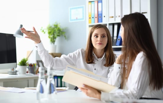 Portrait of pretty businesswoman sitting indoors and talking about important profitable project with friendly female manager. Accounting workplace concept
