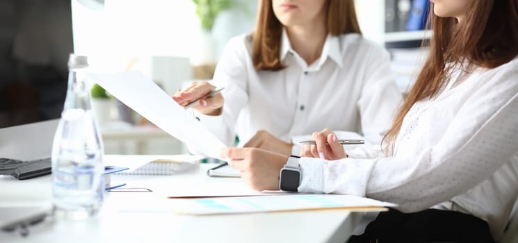 Focus on woman holding metallic writing pen and sitting with friendly colleague discussing something important. Businesswoman arm in watches. Accounting workplace concept. Blurred background