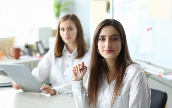 Portrait of joyful businesswoman sitting in modern workplace and looking at camera with calmness. Pretty woman discussing important important profitable strategy. Accounting workplace concept