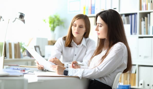 Portrait of joyful businesswoman sitting indoors with friendly colleague and looking at important project in paper folder with charts and graphs. Accounting office concept