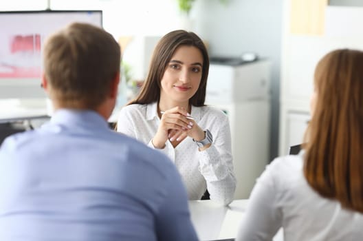 Portrait of smart businesswoman sitting in front of friendly customers and looking at people with concentration and calmness. Office interior. Biz meeting concept