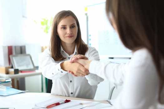 Portrait of smiling businesswoman sitting at comfortable workplace and performing corporation gesture to show mutual professional affection. Accounting office concept