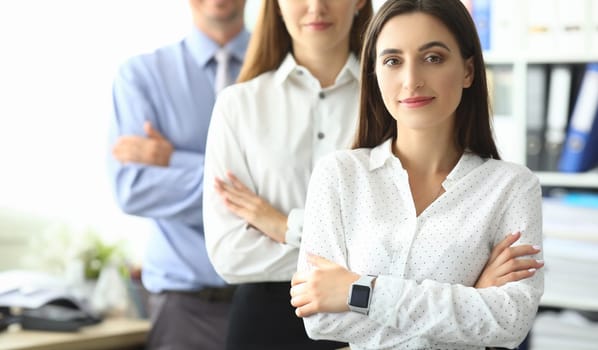 Portrait of joyful managers standing at modern workplace and looking at camera with calmness and concentration. Smiling lady standing with businesspeople. Friendly teamwork concept