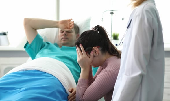 Girl crying near man lying on bed in ward clinic. Monitoring all vital functions patient. Medicine use modern and proven practice diagnostic and treatment methods. Preoperative preparation