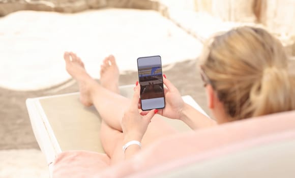Young woman lying on sun lounger on beach and taking pictures of her feet on mobile phone closeup. Photo on social networks concept
