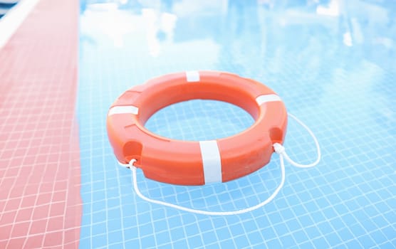 Orange plastic lifebuoy floating in pool closeup. Safety on water concept