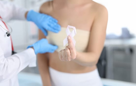 Gynecologist conducts medical examination of female breast. Woman holding pink ribbon in hand concept
