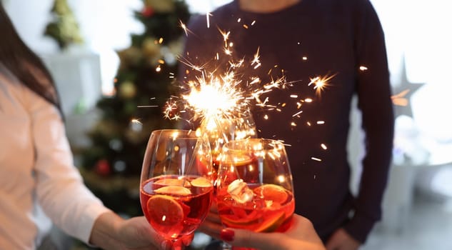 Three glasses with cocktails and sparklers on background of New Year tree. Christmas party concept