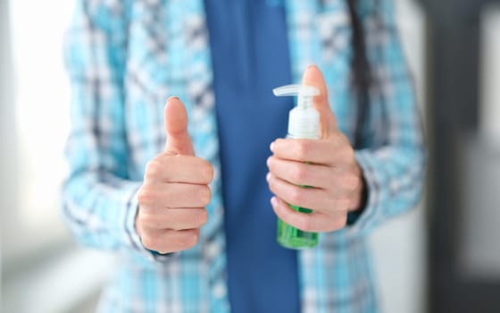 Woman holding disinfectant gesture thumbs up. Approved hand hygiene products concept