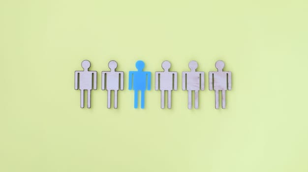 Figures of beige wooden little men in middle one blue. Human personality concept