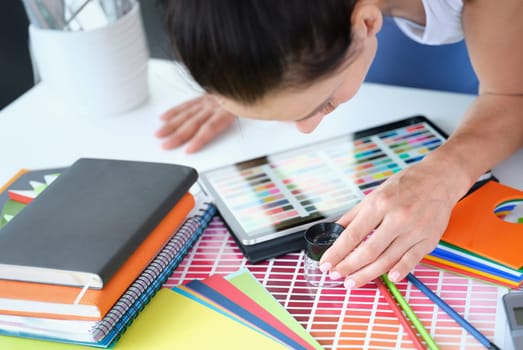 Woman designer looks through magnifying glass at color palette with different shades of colors. Color matching concept