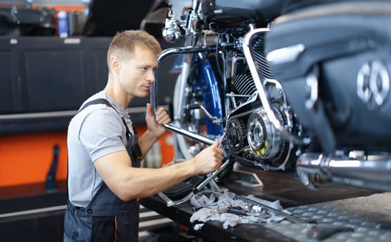 Male car mechanic holds wrench and looks at open motorcycle engine. High-quality motorcycle repair and maintenance concept