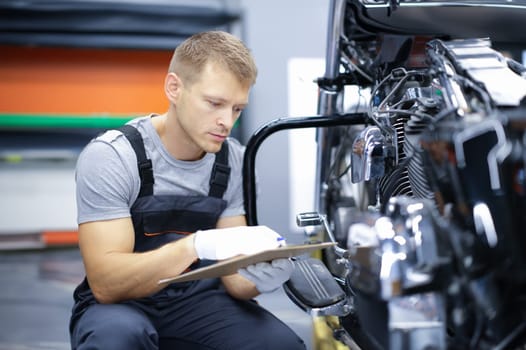 Young car mechanic conducts diagnostics of motorcycle engine in car service. Car and motorcycle warranty service concept