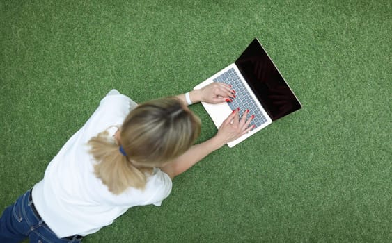 Young woman lying on green grass and typing on laptop keyboard top view. Communication on social networks concept