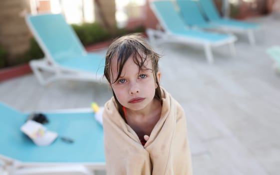 Little frozen girl in towel standing near swimming pool. Hypothermia in children concept