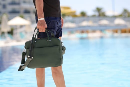 Man with bag for documents walking along edge of swimming pool closeup. Business work at resort concept