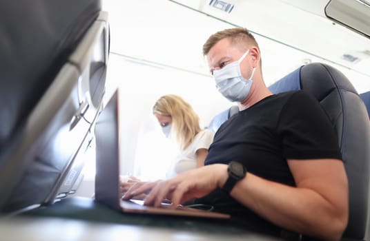 Man and woman in protective masks working on laptops in aircraft cabin. Teleworking during covid19 pandemic concept
