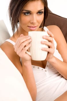 Young female resting on sofa in white vest top, dring from a mug.