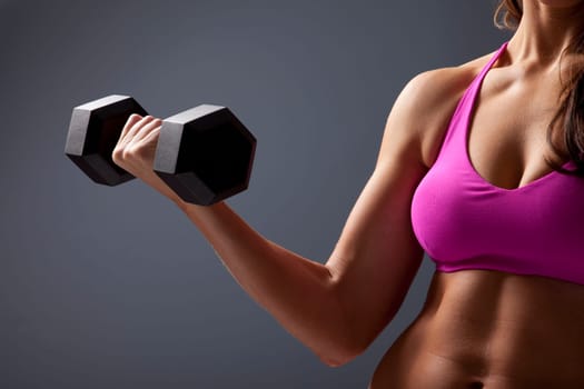 Studio close up photo of young woman lifting dumbbell.