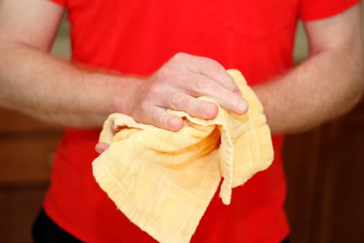 Adult male caucasian wearing a red shirt drying hands on a yellow cotton cloth dish towel close up.