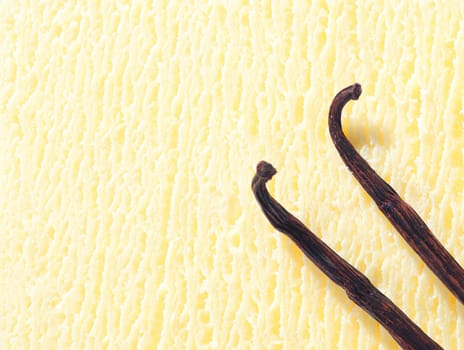 Closeup of a creamy icecream texture with two dried vanilla pods used as a flavouring during preparation