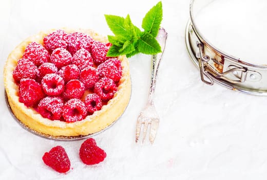 High angle view of a delicious freshly baked raspberry pie in a golden pie crust garnished with a sprig of mint and served with a silver fork