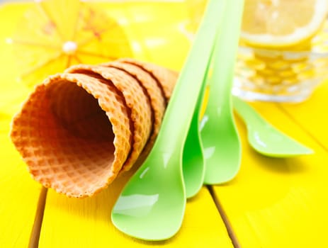 Closeup of a stack of four empty sugar wafer icecream cones with green plastic spoons on a wooden yellow tabletop