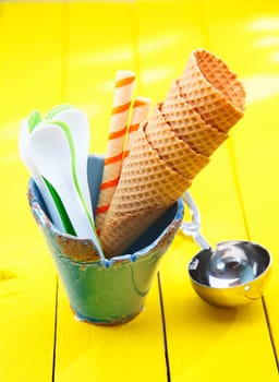 Catering still life with stacked sugar wafer icecream cones and spoons in a pottery container alongside a metal icecream scoop