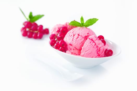 Serving of gourmet redcurrant icecream topped with fresh whole redcurrants and garnished with mint on a white background