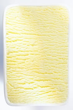 Closeup vertical background texture of a tub of lemon sorbet or vanilla icecream with a shadowed ripple running through the centre