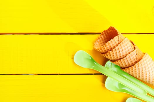 Ice cream cones and green plastic spoons on yellow table with copy space