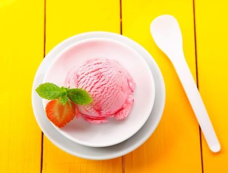 Overhead view of a round ball serving of creamy strawberry icecream served in a circular bowl on yellow table