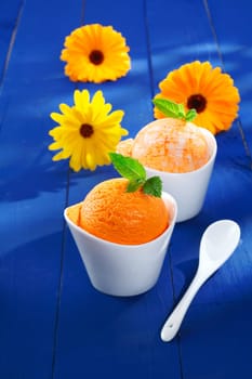 Refreshing orange and mango icecream dessert served in indivual little bowls with colourful summer gerbera daisies on blue wooden boards. For ice-cream concept look at my portfolio