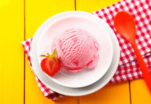 Overhead view of a country meal of strawberry icecream served on a colourful red and white checkered napkin on a yellow wooden tabletop